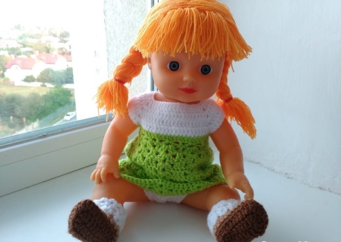 Кукла с рыжими косичками в вязаном бело-зелёном платье на окне